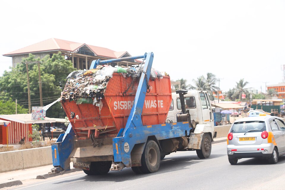 Skip-loader refuse truck carrying waste along an urban road